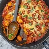 Gnocchi baked with tomato sauce, melted cheese, pepperoni slices, grated parmesan, and fresh basil on a marble surface.
