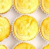 Nine golden-yellow cupcakes in white paper liners arranged closely on a white surface.
