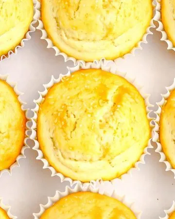 Nine golden-yellow cupcakes in white paper liners arranged closely on a white surface.