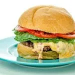 Cheeseburger with lettuce and tomato on a blue plate, cheese melting over the beef patty.