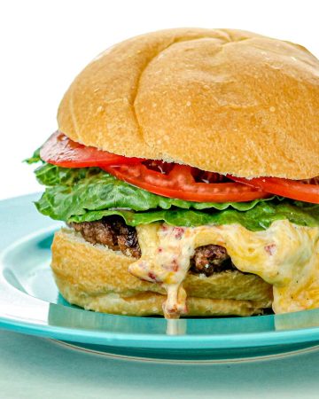 Cheeseburger with lettuce and tomato on a blue plate, cheese melting over the beef patty.