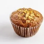 Banana nut muffin with chopped walnuts on top in a brown paper liner against white background.