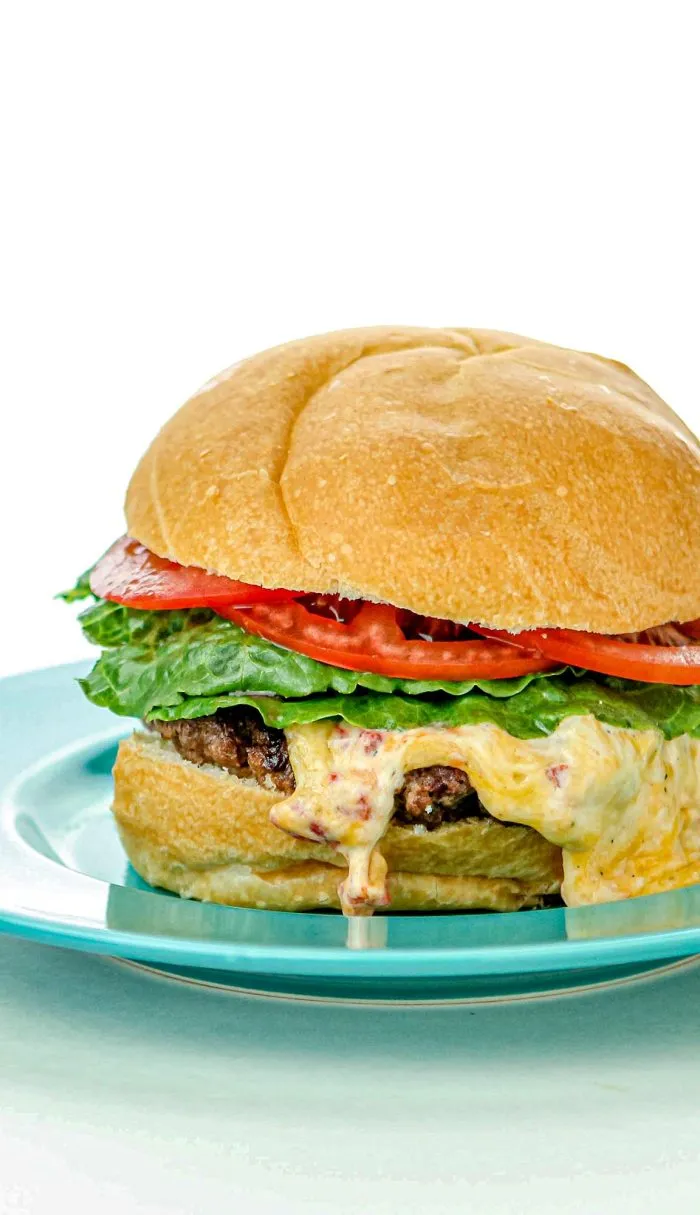 Cheeseburger with lettuce, tomato, melted cheese, and beef patty on a blue plate with a white background.