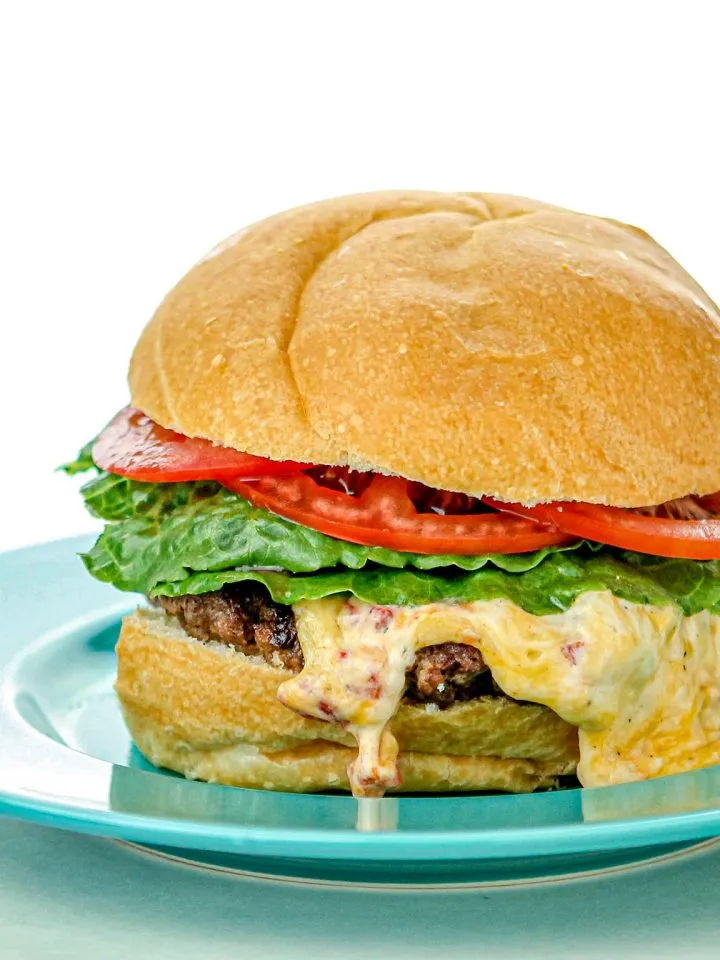 Cheeseburger with lettuce, tomato, melted cheese, and beef patty on a blue plate with a white background.